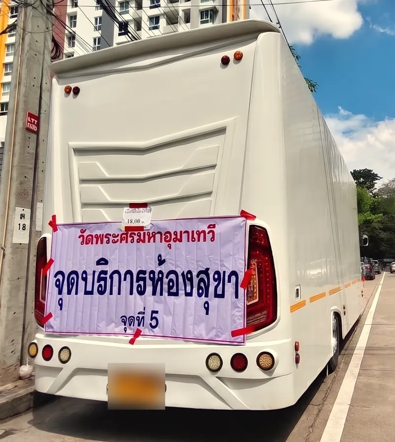 ท้ายรถสุขาเคลื่อนที่ทรงโค้งสีขาว ติดป้าย จุดบริการห้องสุขา จุดที่ 5 ริมถนน